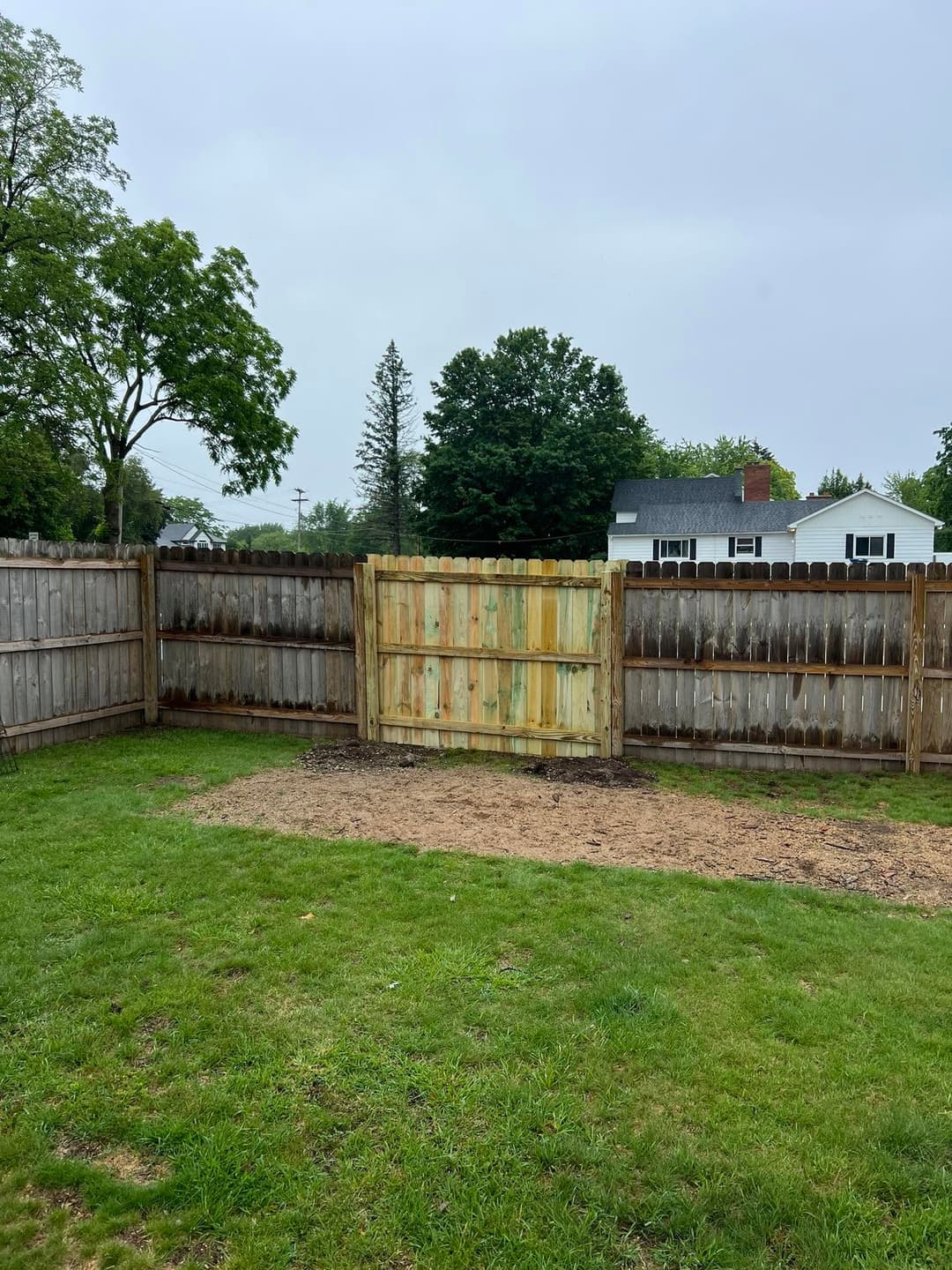 Wooden gate in a fenced backyard with grass and a cloudy sky. Ideal for garden security.