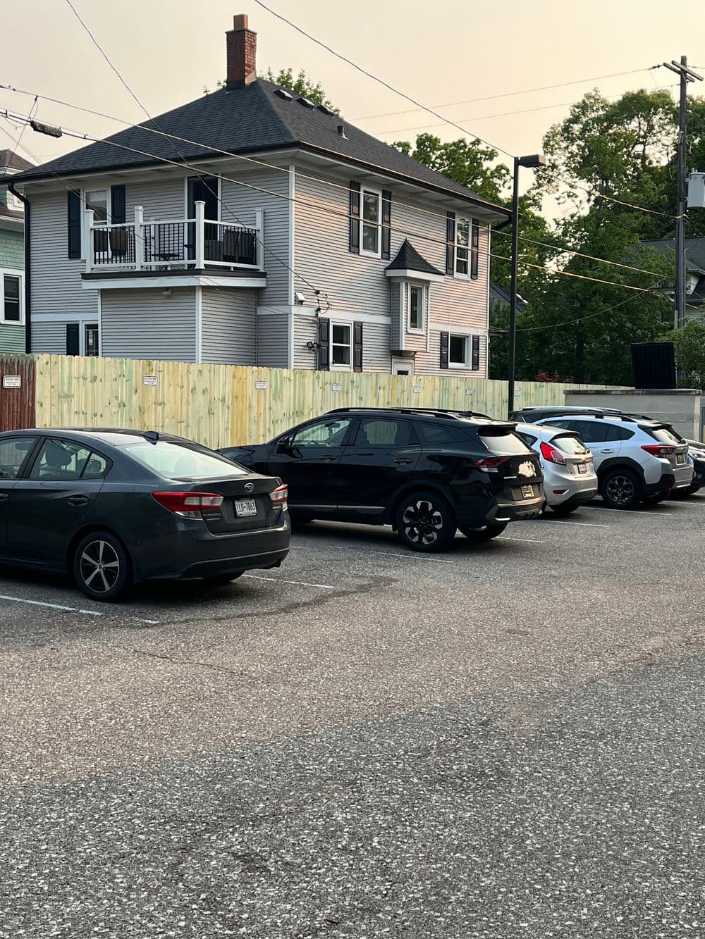 Cars parked in a lot near a two-story residential building with a wooden fence.