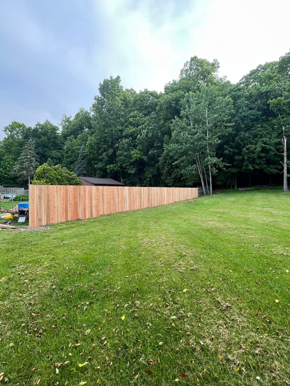 New wooden fence in a spacious green yard surrounded by trees.