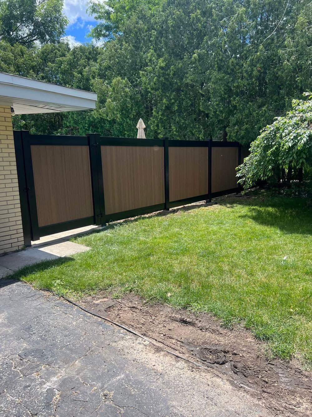 Vinyl privacy fence with brown panels in a residential backyard with green grass.