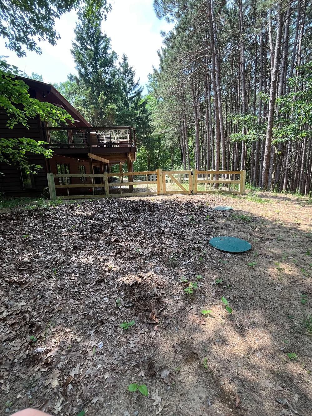 Wooded backyard with a house, wooden fence, and fallen leaves in a serene setting.